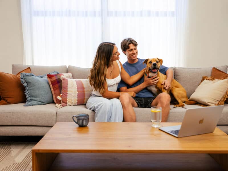 First home buyers sit on the couch with their dog in their first home. Builds by Step1 Homes, backed by Plunkett Homes.
